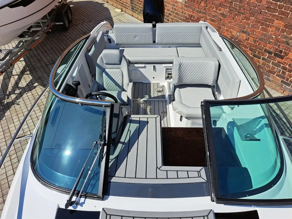 Top view of a modern boat interior featuring grey upholstered seats, a steering wheel, and a glass windshield.